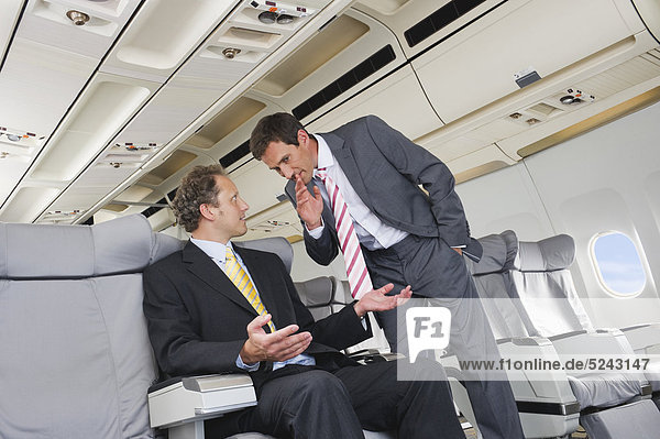 Germany  Bavaria  Munich  Businessmen whispering in business class airplane cabin