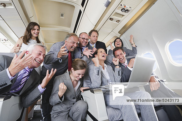 Germany  Bavaria  Munich  Group of passengers looking in laptop in business class airplane cabin  laughing