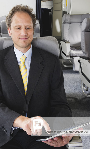 Deutschland  Bayern  München  Geschäftsmann mit ipad in der Business Class Flugzeugkabine  lächelnd