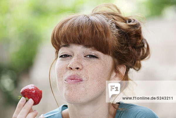 Nahaufnahme einer jungen Frau  die Erdbeere isst  lächelnd  Portrait