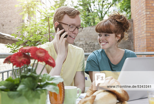 Germany  Berlin  Young couple using cell phone and laptop  smiling