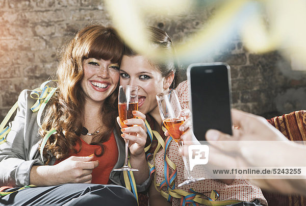 Junge Frauen halten Champagnerglas und Mann fotografiert mit Handy  lächelnd