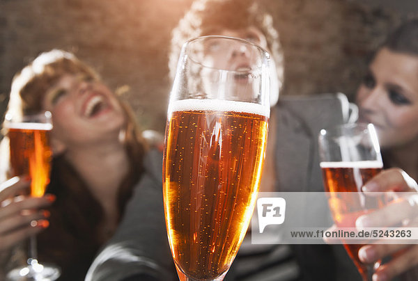 Deutschland  Berlin  Nahaufnahme eines Champagnerglases vor Freunden beim Feiern  lächeln