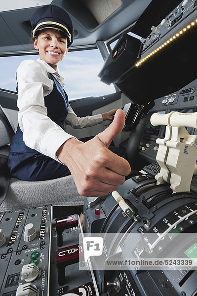 Woman flight captain with thumbs up in airplane cockpit
