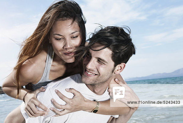 Spanien  Mallorca  Junger Mann mit Frau auf dem Rücken am Strand