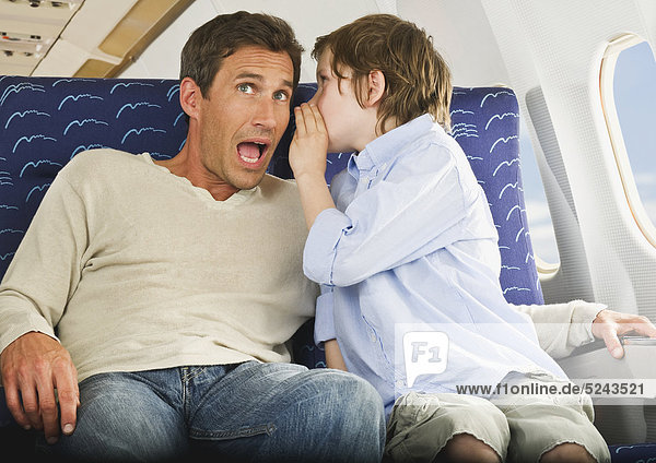 Boy whispering in man's ear in economy class airliner