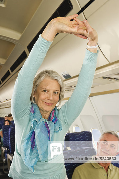 Senior woman stretching and man looking in economy class airliner