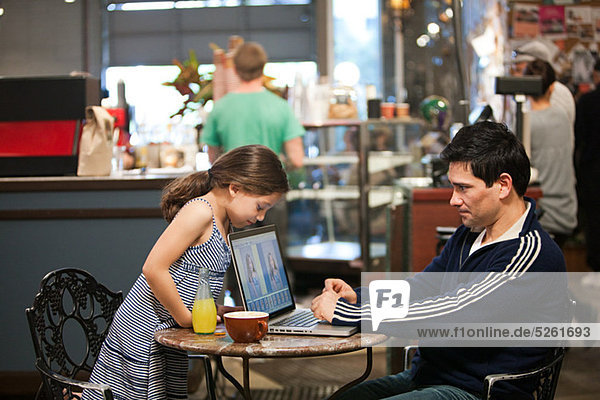Father and daughter with laptop in cafe