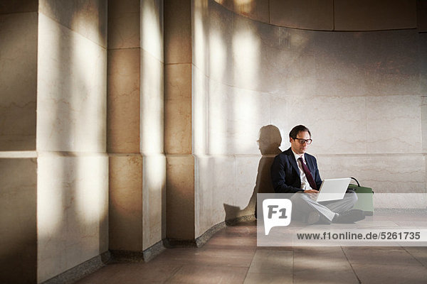 Businessman sitting on floor by wall using laptop