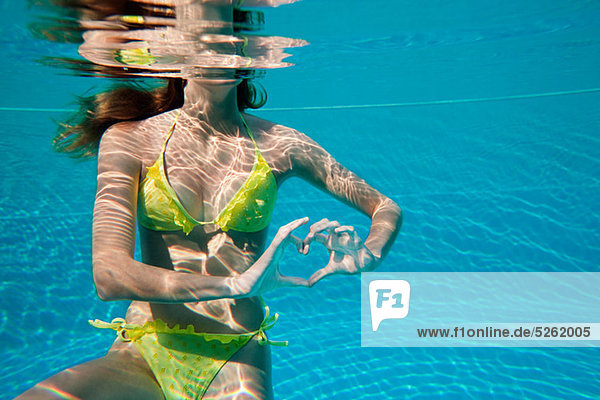 Young woman making heart shape with hands underwater in swimming pool