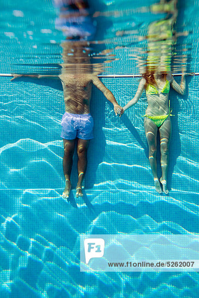 Young couple holding hands in swimming pool  underwater view