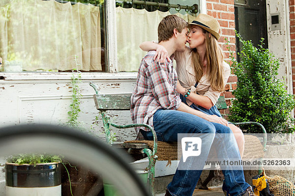 Junges Paar küsst sich auf der Bank