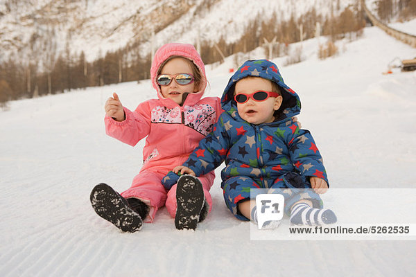 Porträt von Bruder und Schwester im Schnee sitzend