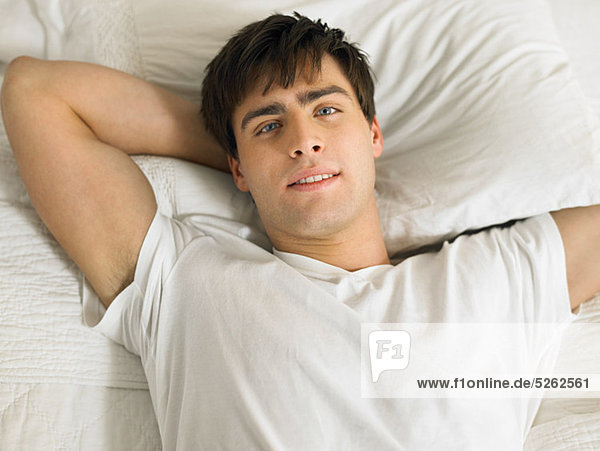 Young man lying on bed with hands behind head  portrait