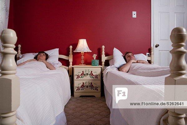 Young couple lying awake in single beds