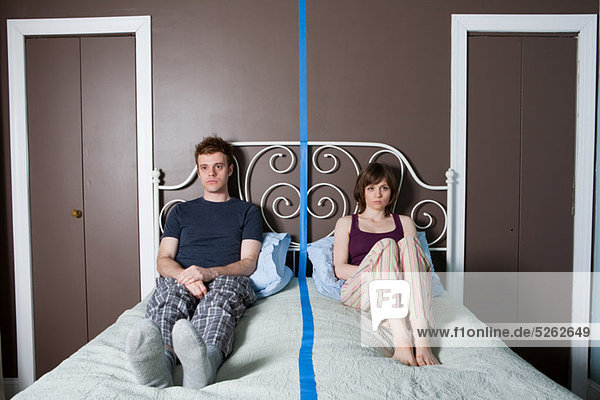 Junges Paar auf dem Bett sitzend  durch blaue Linie getrennt