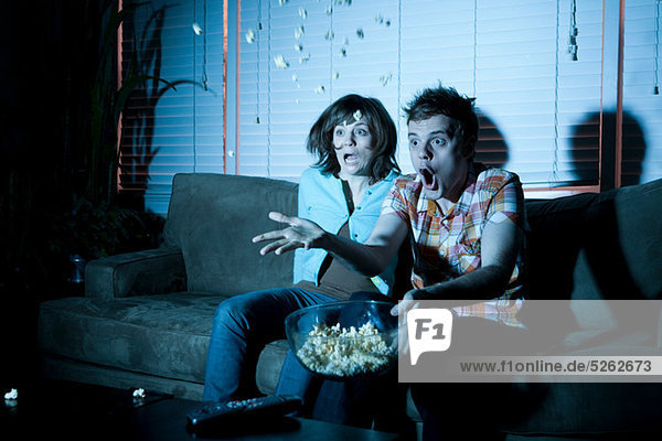 Junges Paar sieht fern  Mann wirft Popcorn