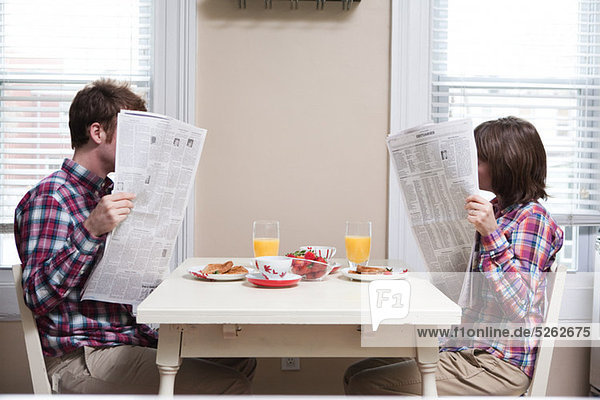 Young couple reading newspapers at kitchen table