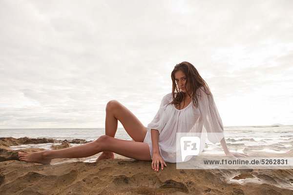 Young woman wearing white top sitting on sand  portrait