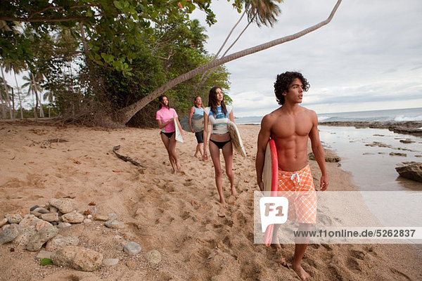 Four young friends carrying surfboards on beach