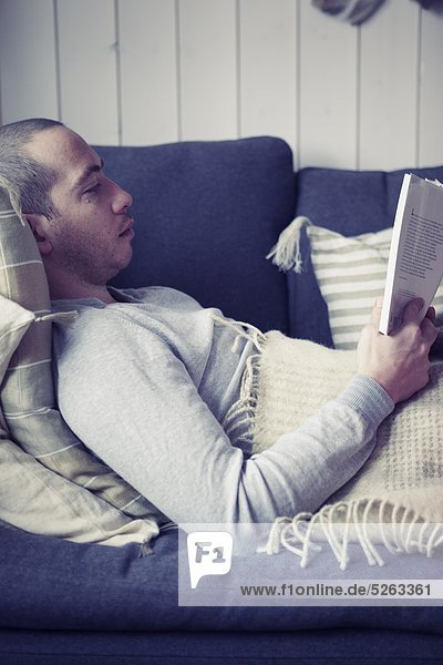 Mann liegt auf einer Couch und liest ein Buch
