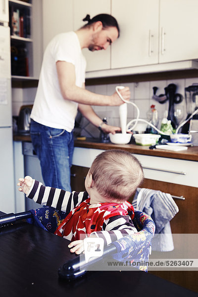 Baby Boy sitzen in Hochstuhl Blick auf Vater  die Zubereitung von Essen