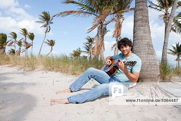 Young man playing guitar on beach  portrait