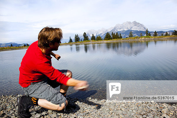 Crouching man throwing stones into a lake
