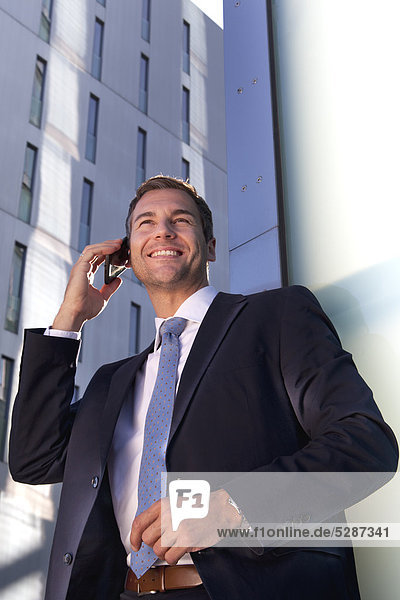 Lächelnder Geschäftsmann telefoniert mit Handy im Freien