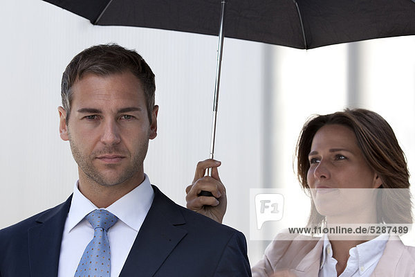 Geschäftsfrau hält einen Regenschirm über einen Geschäftsmann