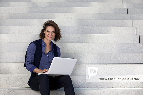 Geschäftsfrau benutzt einen Laptop auf einer Treppe