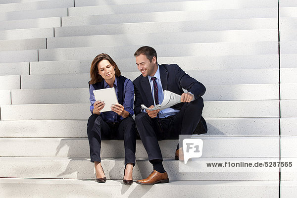 Geschäftsmann und Geschäftsfrau mit Tablet PC und Zeitung auf einer Treppe