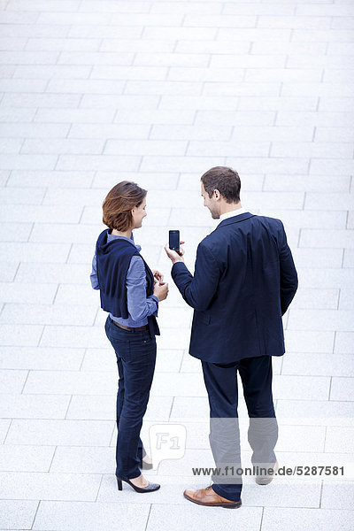 Geschäftsmann und Geschäftsfrau stehen mit Handy im Freien