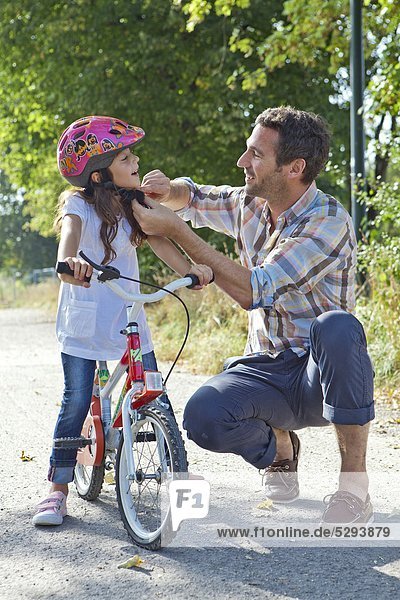 Father closing the helmet of her daughter on a bike