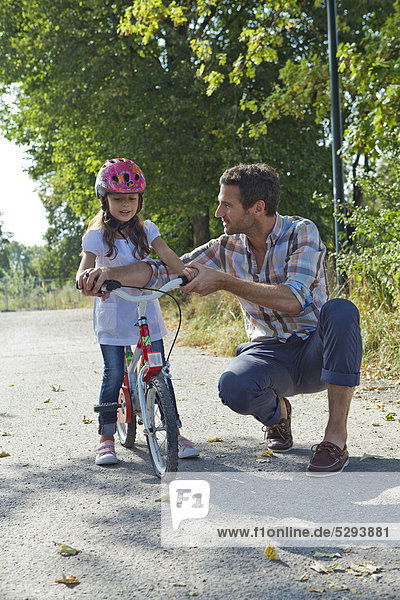Vater und Tochter mit Helm auf Fahrrad im Freien