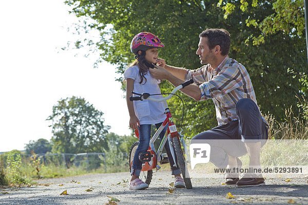Father closing the helmet of her daughter on a bike