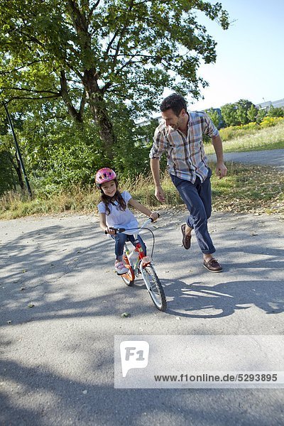 Father running next to daughter on bike