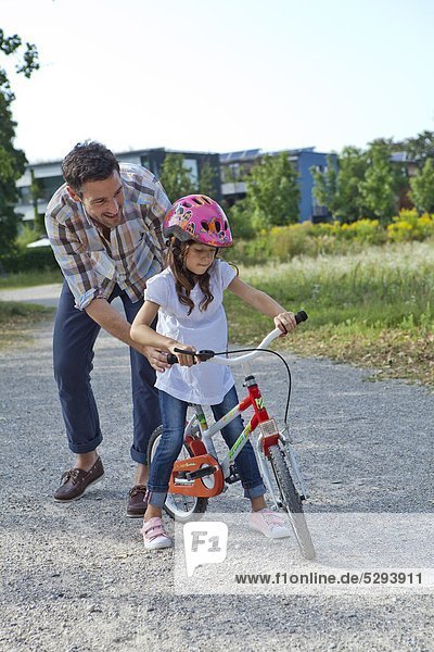 Vater hält Tochter auf Fahrrad im Freien