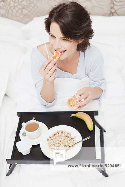 Lächelnde Frau beim Frühstück im Bett
