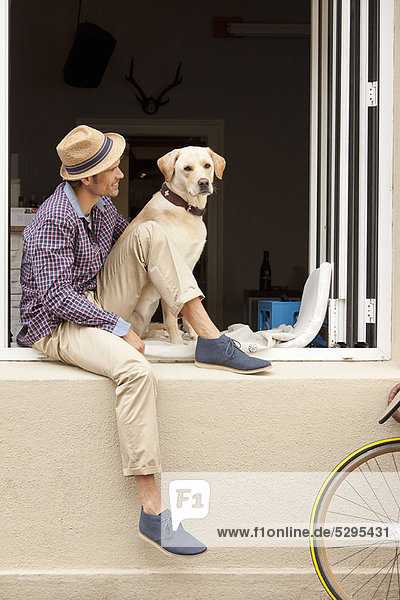 Mann sitzend mit Hund auf der Fensterbank