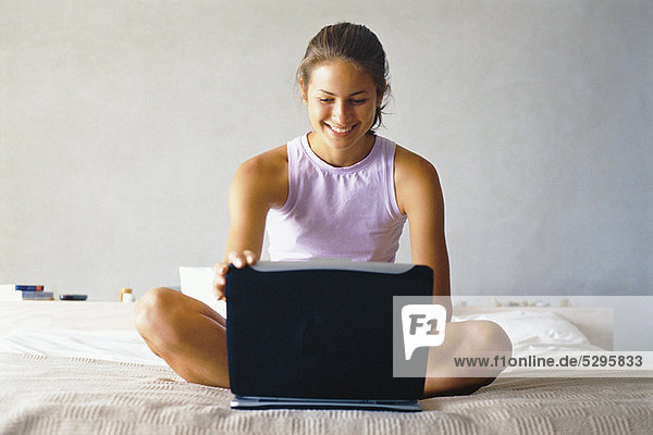 Smiling woman using laptop on bed