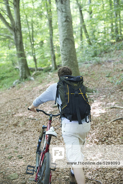 Man pushing bicycle in woods  rear view