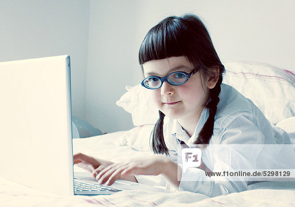 Girl lying on bed using laptop computer