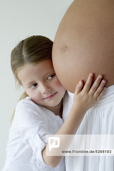 Mädchen  das den schwangeren Bauch der Mutter umarmt.