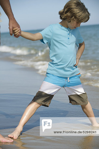 Junge steht mit auseinander stehenden Beinen im nassen Sand am Strand