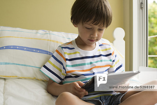 Boy sitting on bed  using digital tablet
