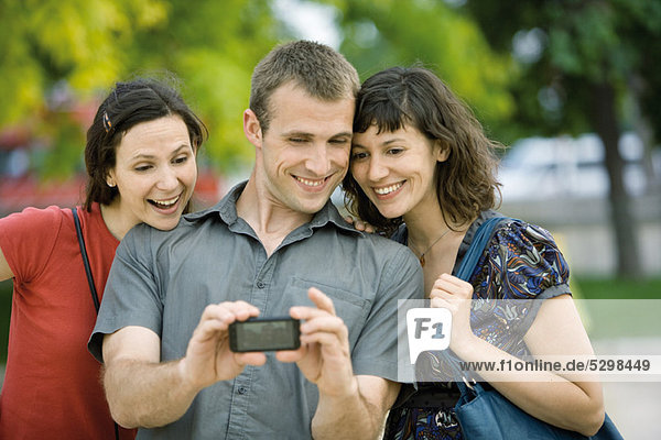 Man photographing himself with two female friends using cell phone