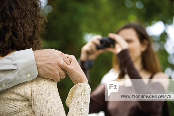 Paar hält sich an den Händen  während die Frau sie fotografiert.
