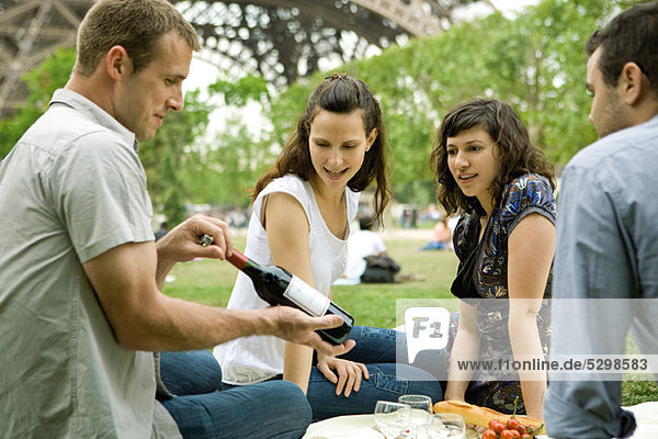 Friends enjoying picnic outdoors  admiring bottle of wine
