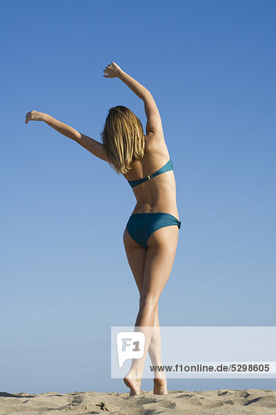 Woman walking on beach with arms raised in air  rear view